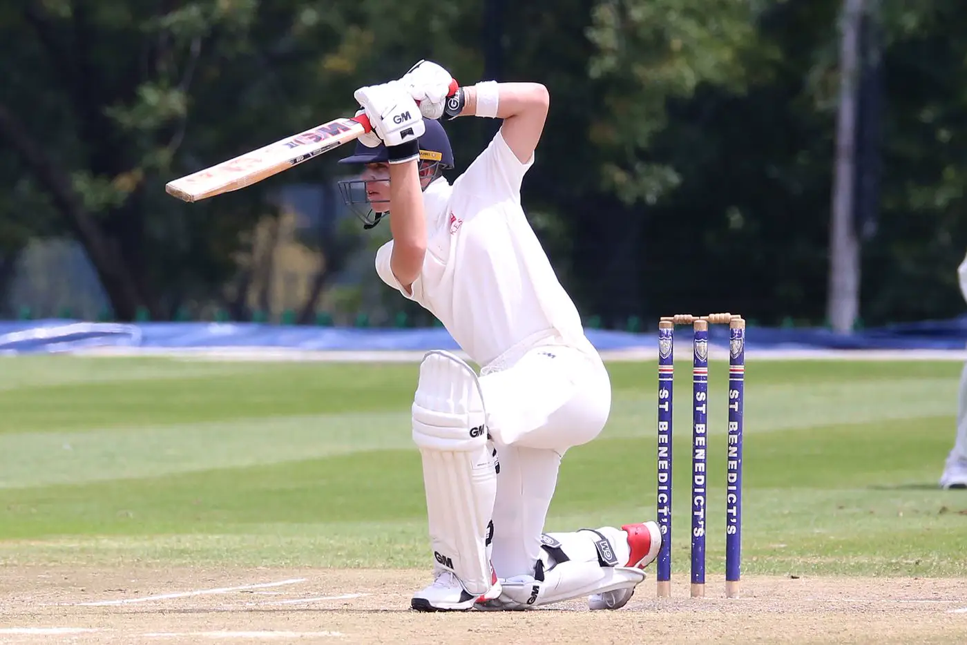 Batter playing a sweep shot in cricket whites